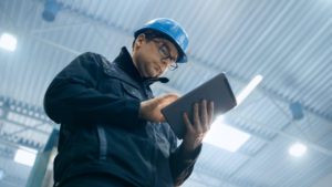 Manufacturing worker with blue hard hat and tablet